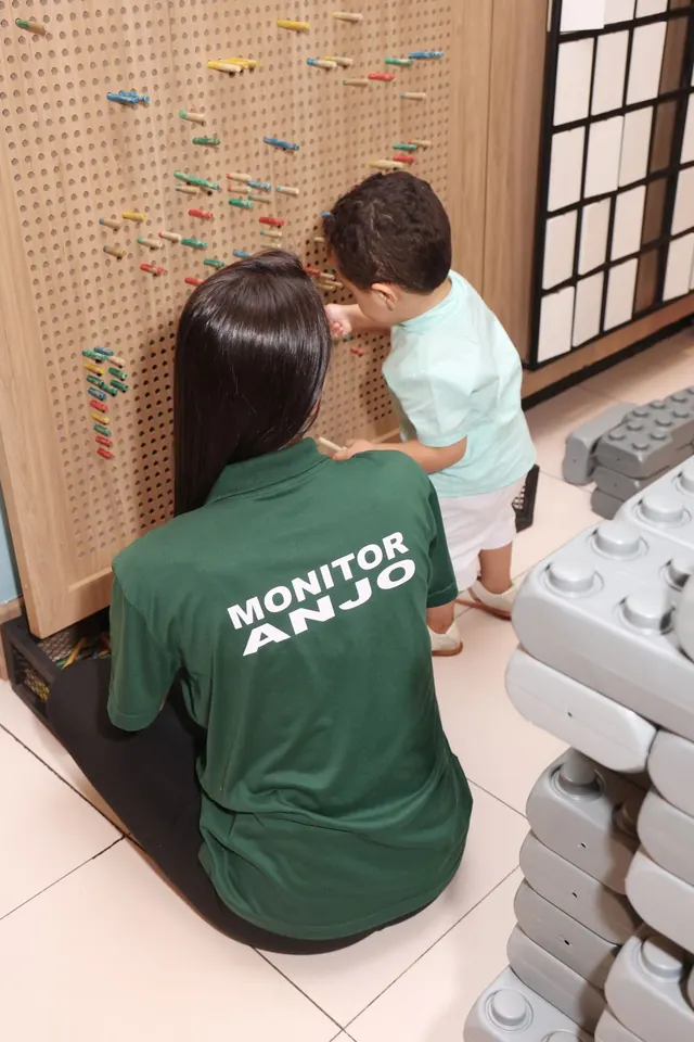 Monitora do Espaço Panda acompanhando um menino no painel de pinos coloridos
