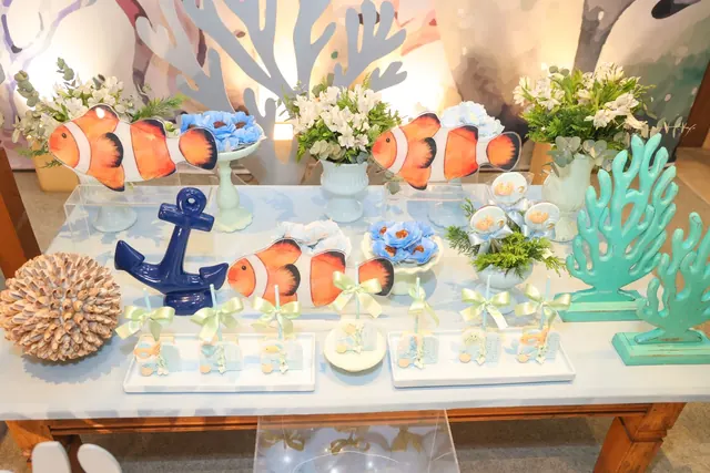 Mesa de doces decorada com peixes-palhaço, âncora e arranjos de flores brancas