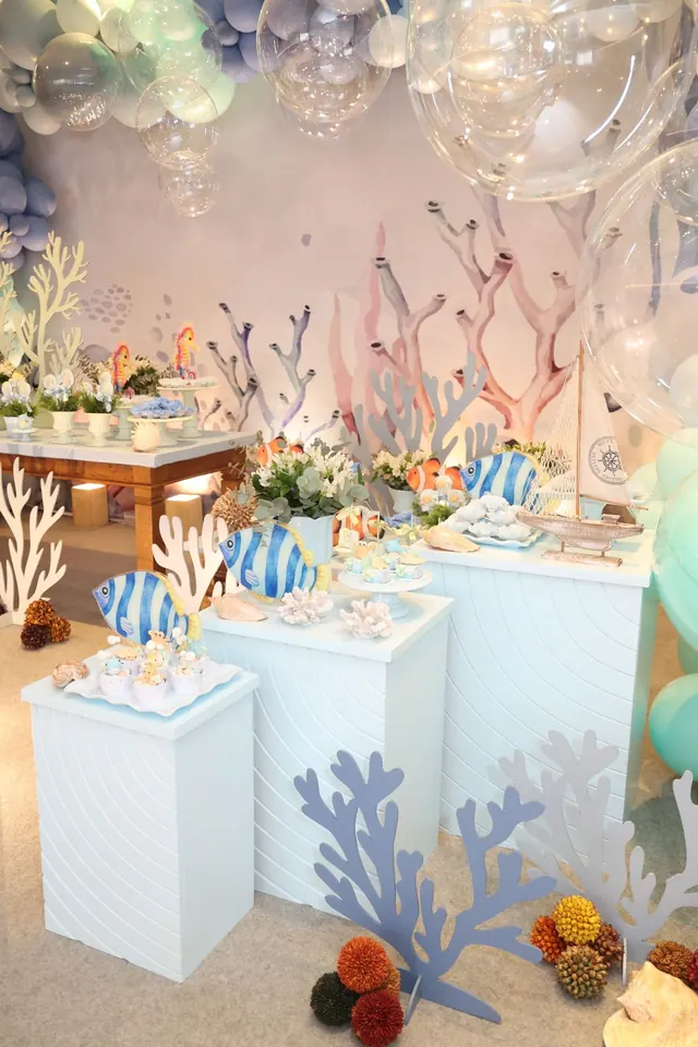 Mesa de doces com peixes listrados, veleiro e corais sobre módulos brancos
