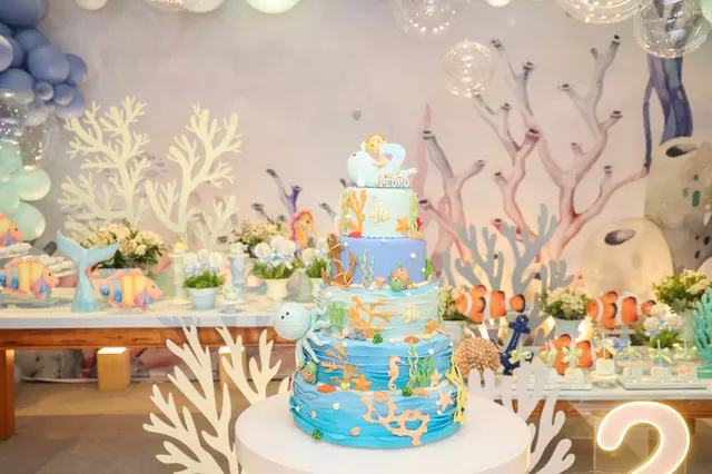 Bolo temático em frente à mesa do parabéns decorada com corais e peixes