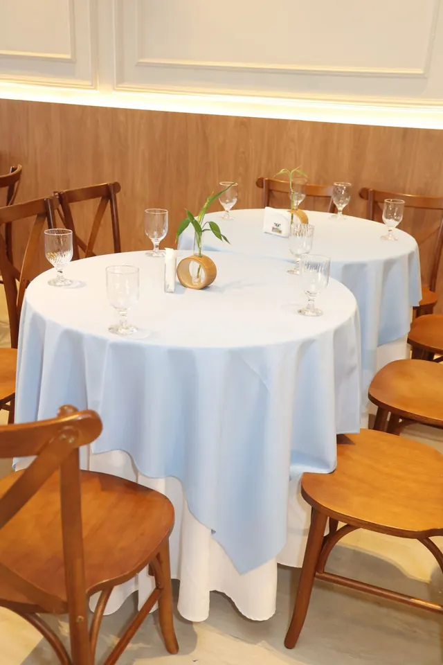 Mesas para convidados com toalhas azuis, taças e centro de mesa com bambu
